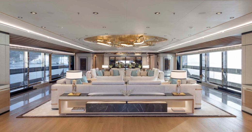 Overview of the main salon onboard charter yacht MALIA with spacious lounge arrangement center and many large windows surrounding 