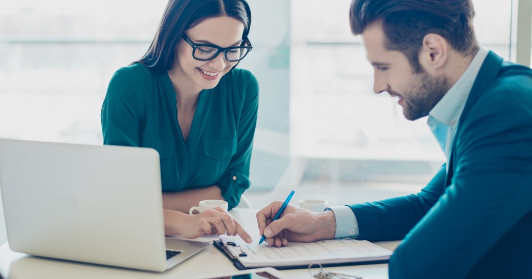 A man signs a document with a professional woman and laptop