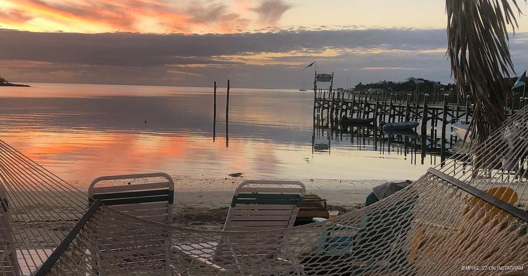 Sun setting over the water while hammocks and sun loungers are set up on the beach 