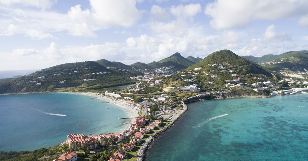 saint martin on a beautiful day in summer with tranquil waters to one side of it and a luxury yacht cruising ground to the other