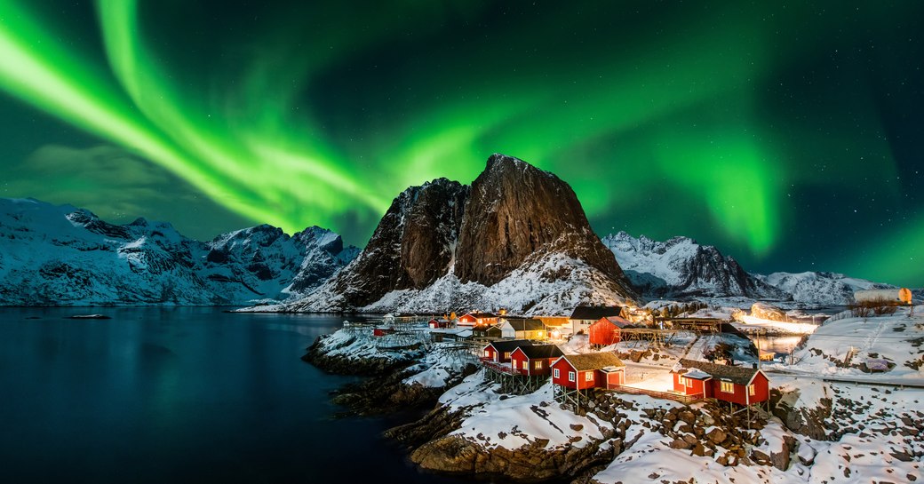 northern lights above town next to the water in norway