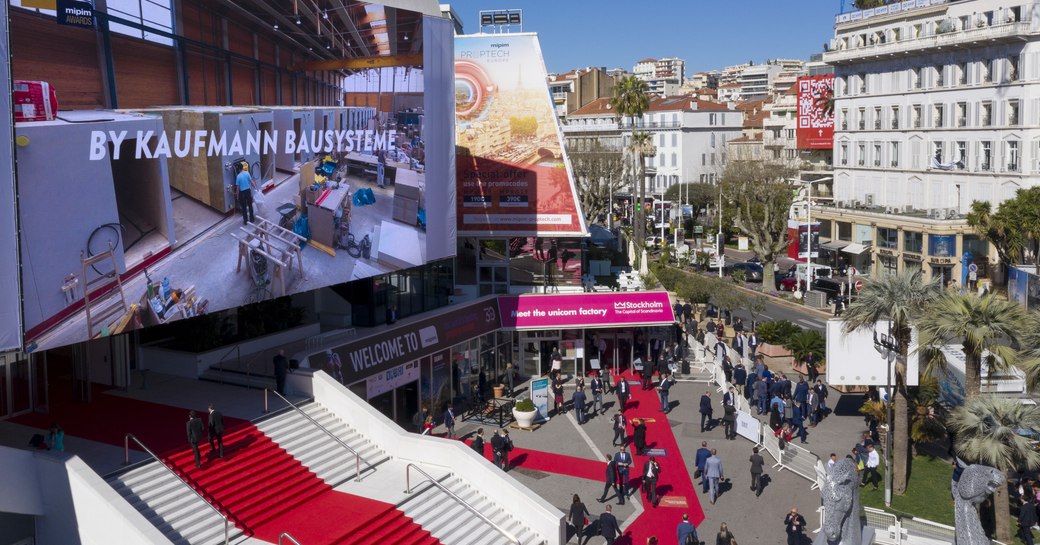 Red carpet entrance to MIPIM Cannes event, surrounded by Cannes infrastructure and visitors ascending steps.