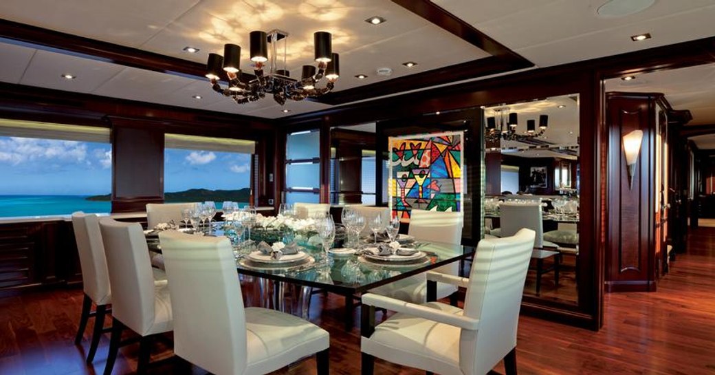 formal dining indoors on charter yacht alessandra, with chandelier above and contemporary art on wall in background, plenty of glass laid out on table