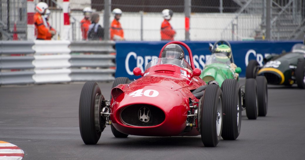 Frontal view of Monaco Historic Grand Prix race in action, three vintage cars on track, overlooked by crew behind barriers.