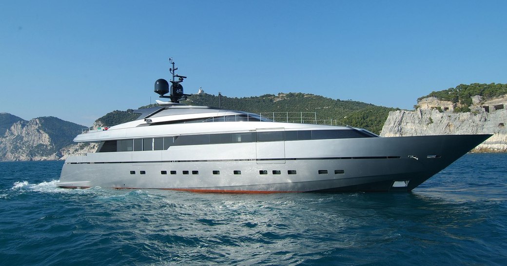 Charter yacht NAIA underway at sea, with cliffs in the background