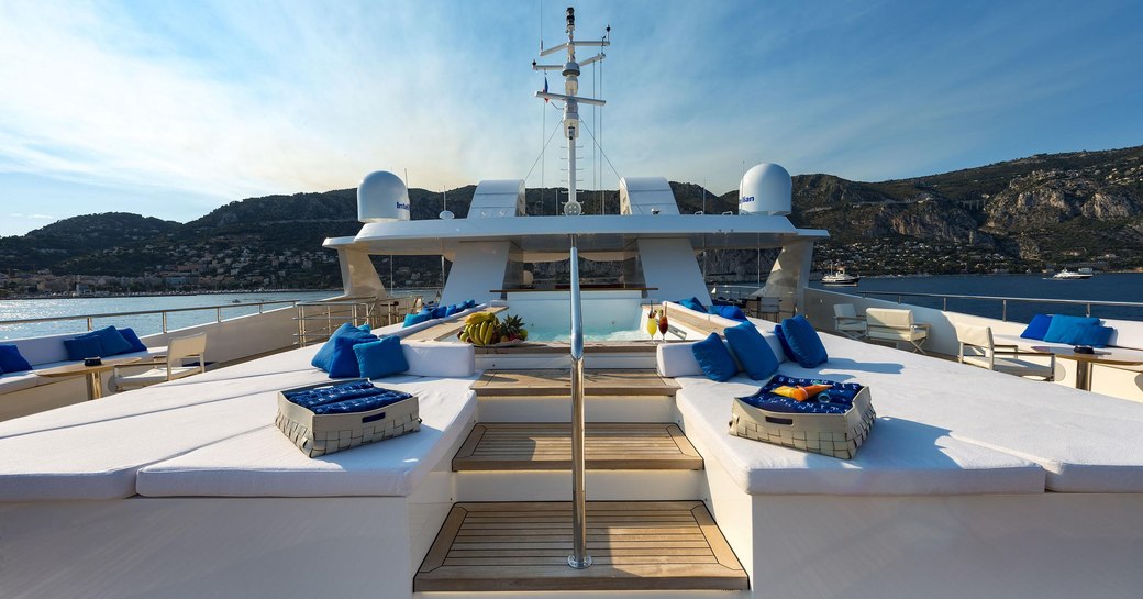 Overview of sun deck onboard M/Y SERENITY, central pool with sun pads in foreground, overlooking elevated terrain in background