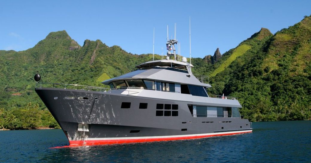 Superyacht AKIKO sits at anchor a short distance from a green coast