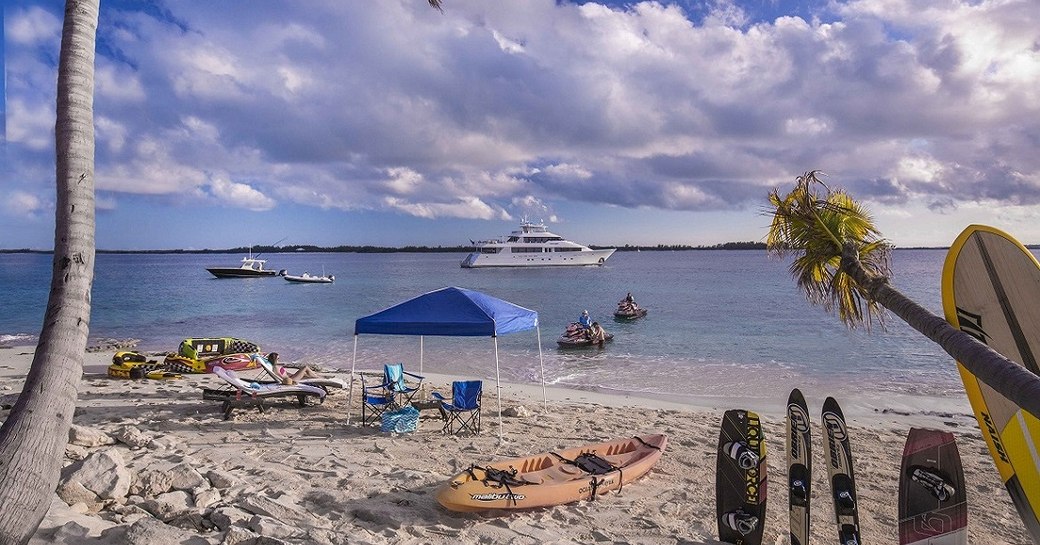 Beach in the Bahamas looking out over water toys in the sand, with charter yacht AMITIE in background on the ocean