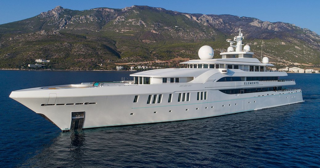 Charter yacht ELEMENTS underway, surrounded by sea with elevated terrain in the background