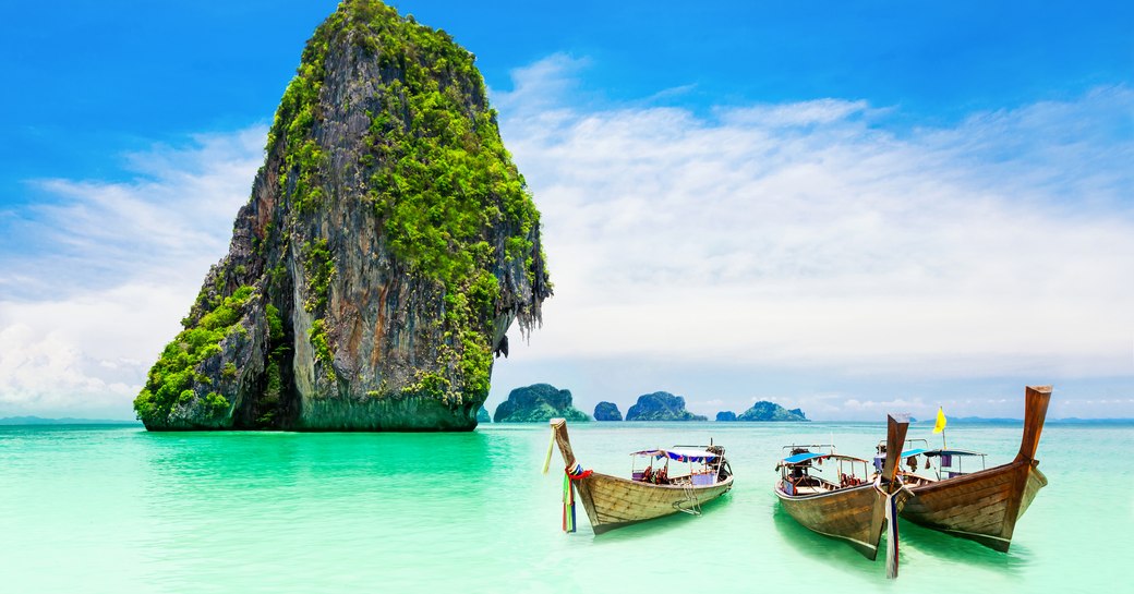 Traditional Thai boats in shallow waters by sandy beach in Thailand