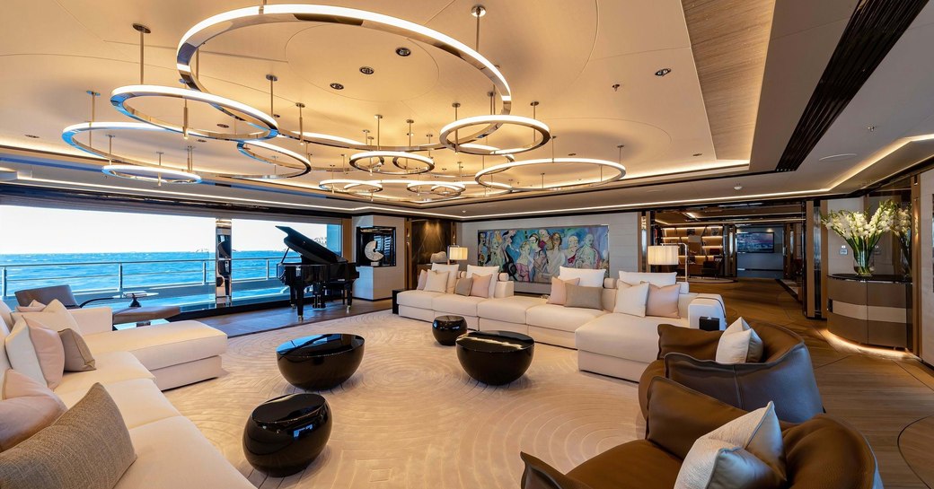 Main salon onboard charter yacht PROJECT X, plush seating arranged by large windows with a grand piano