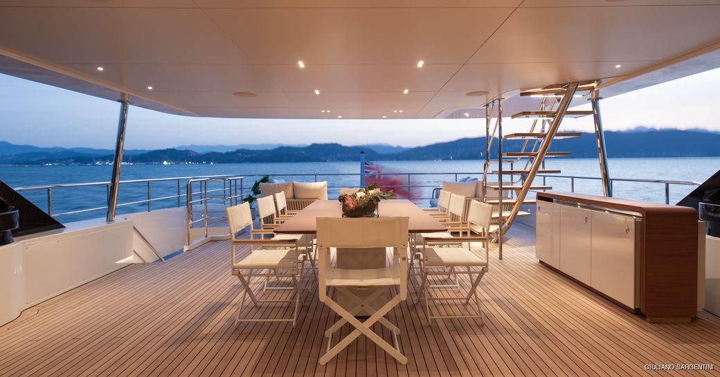 Alfresco dining set up onboard yacht charter LEGEND with a long white table and directors chairs.
