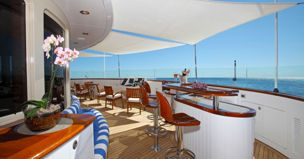 Chairs line a bar beneath shading located on the exterior of a superyacht