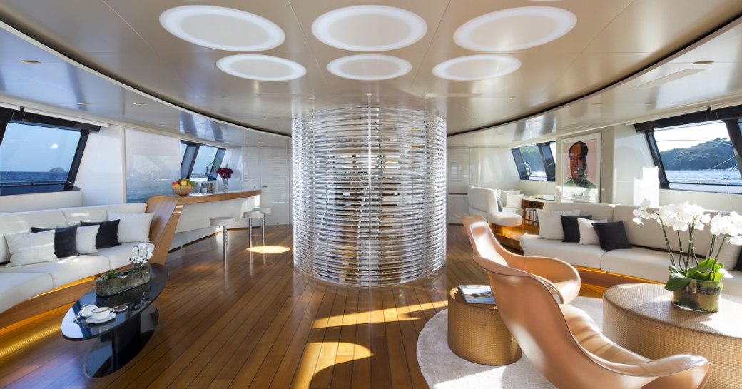 main salon with curved sofas, modern armchair and a central feature staircase aboard charter yacht PANTHALASSA 