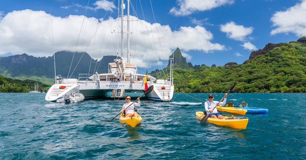 Charter guests in yellow kayaks with catamaran yacht charter DOUCE FRANCE in the background