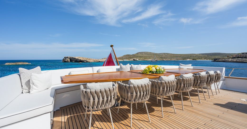 Alfresco long dining table with benched seating on the exterior decks of superyacht charter EMERALD