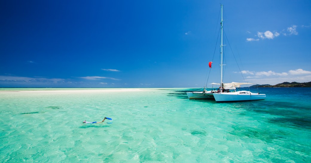 Catamaran at anchor in the Maldives with a snorkeler near the bow