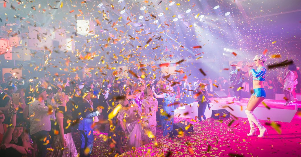 Female performer on stage in front of busy audience dancing, confetti falling all around