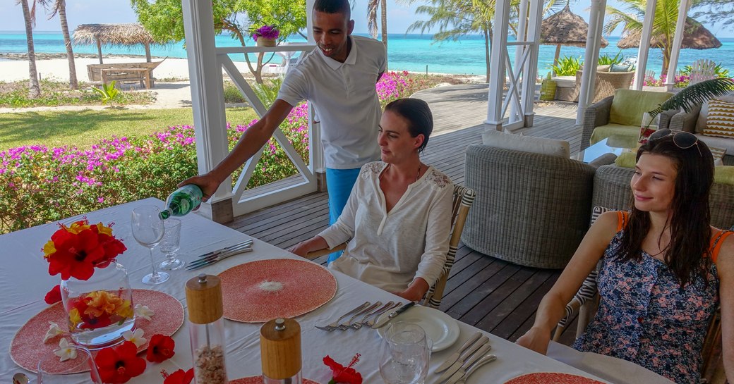 diners enjoying water being served on thanda island, a luxury private island in tanzania with views of beach and palm trees in background