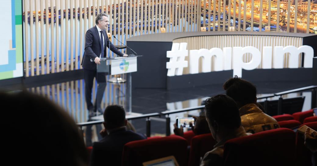 A keynote speaker on stage at a MIPIM conference in Cannes.