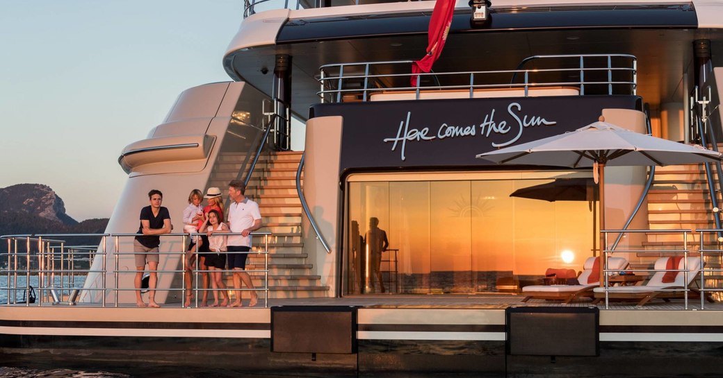 family of charter guests stand on the swim platform of Here Comes The Sun as the sun sets