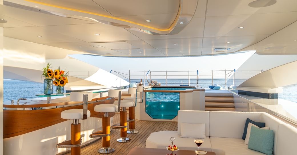 Exterior deck with a port side wet bar, white seating to starboard and a deck Jacuzzi aft onboard charter yacht ETERNAL SPARK