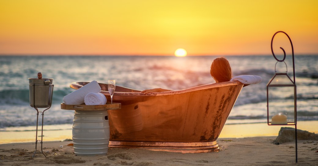 woman relaxes in copper bath on the beach surrounded by lanterns on thanda island