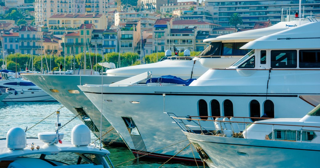 Line of motor yachts moored at Cannes Yachting Festival, Cannes visible in background past bows of yachts.