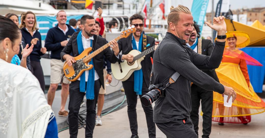 Celebration during MYBA Charter Show at Port Vell, Barcelona. Live band and spectators watch photographer dance.