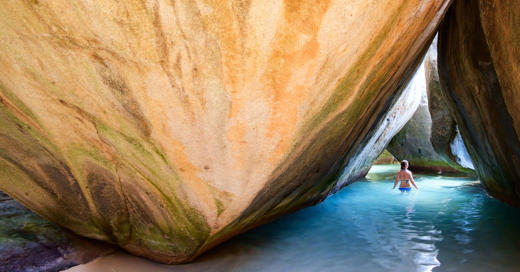 woman drifting through large rock structure by the crystalline waters of the virgin islands