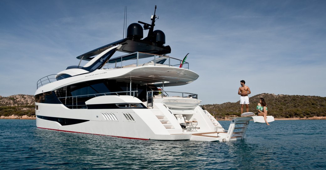 man and woman sit on extendable swim platform of luxury yacht hanaa, looking at yacht