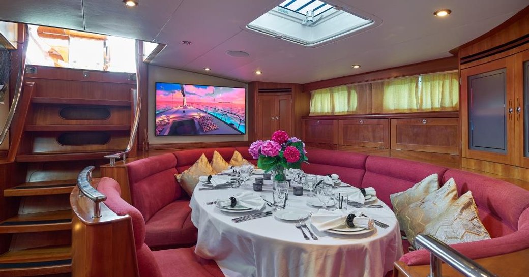 Interior dining setup onboard sailing yacht charter DARK STAR OF LONDON, circular table and surrounding bench seating laid for a meal