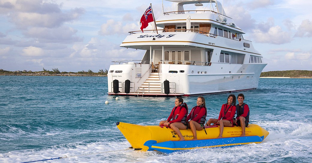 Four charter guests enjoy a banana boat close to superyacht Lady J