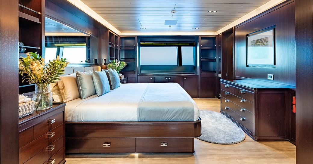 Guest cabin onboard private yacht charter GALILEO, large berth facing starboard with wide window in the background and surrounding storage 