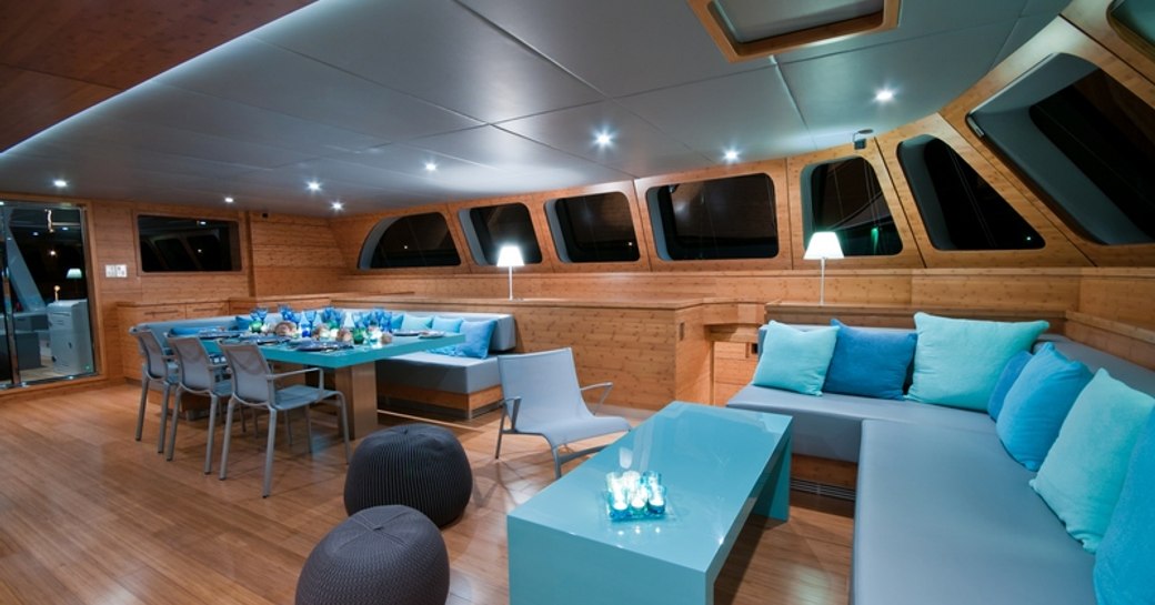 the main salon with adjoining dining area inside superyacht che designed with wood embellishments and turquoise accents 