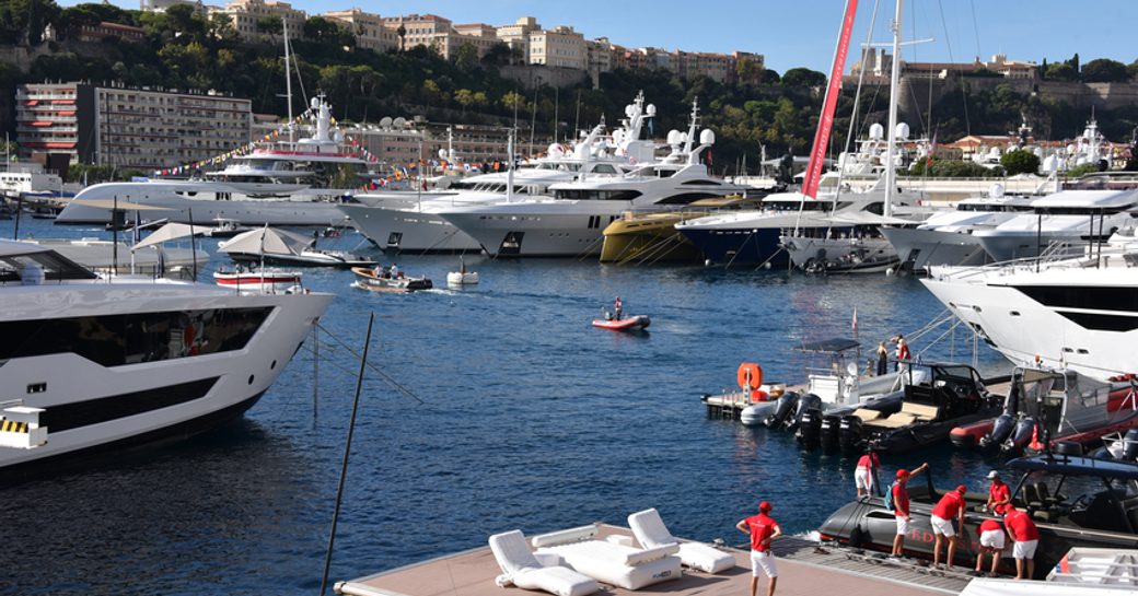 Superyachts moored, with tenders travelling between through Port Hercule, Monaco. Crew onboard nearest yacht awaiting visitors.