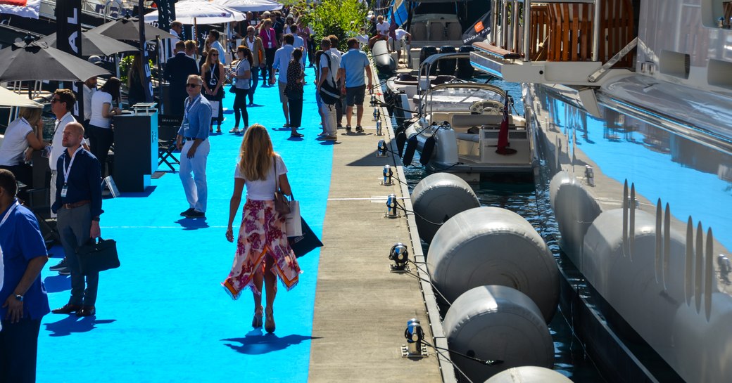 Woman attending the Monaco Yacht Show, walking along the blue carpet alongside superyacht 