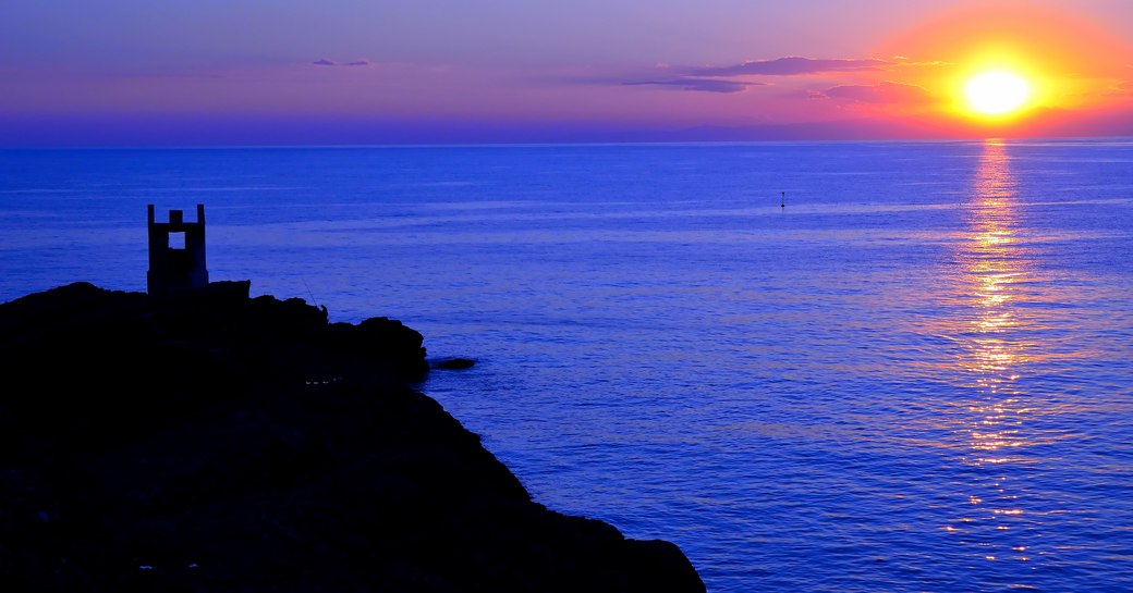 Sun setting on blue sea with castle in foreground