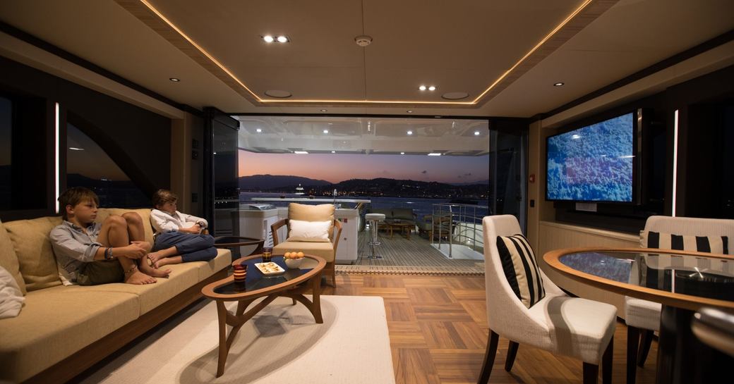 Charter guests watching TV on charter yacht ONEWORLD, with view over sundeck in background