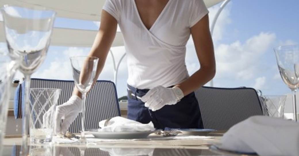 A yacht stewardess lays the table for the evening meal