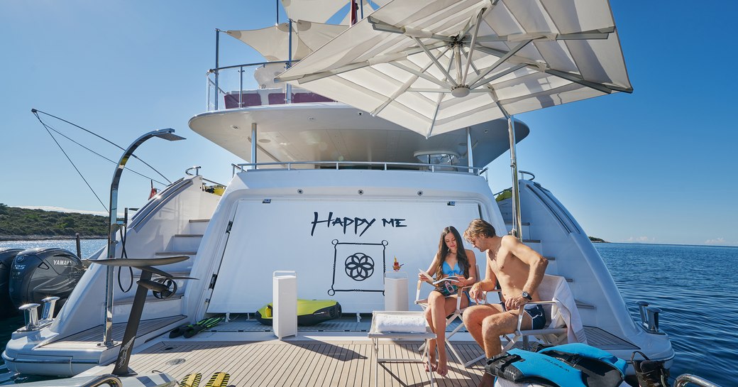 Aft view of charter yacht HAPPY ME. Two charter guests relaxing on seats on the swim platform.