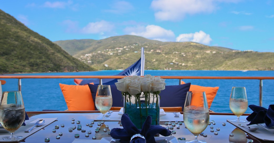 White dining table set with knives, forks, plates and glasses.  Blue and orange cushions in the background on superyacht M4