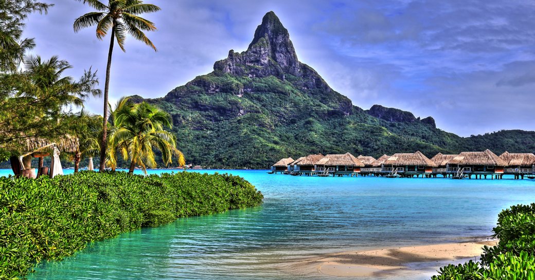 View on Mount Otemanu through turquoise lagoon, palms, and overwater bungalows on the tropical island Bora Bora