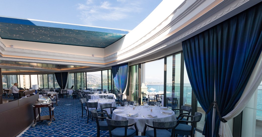 Dining room of Le Grill restaurant in Monaco, with glass ceilings, panoramic views and blue accents around the space