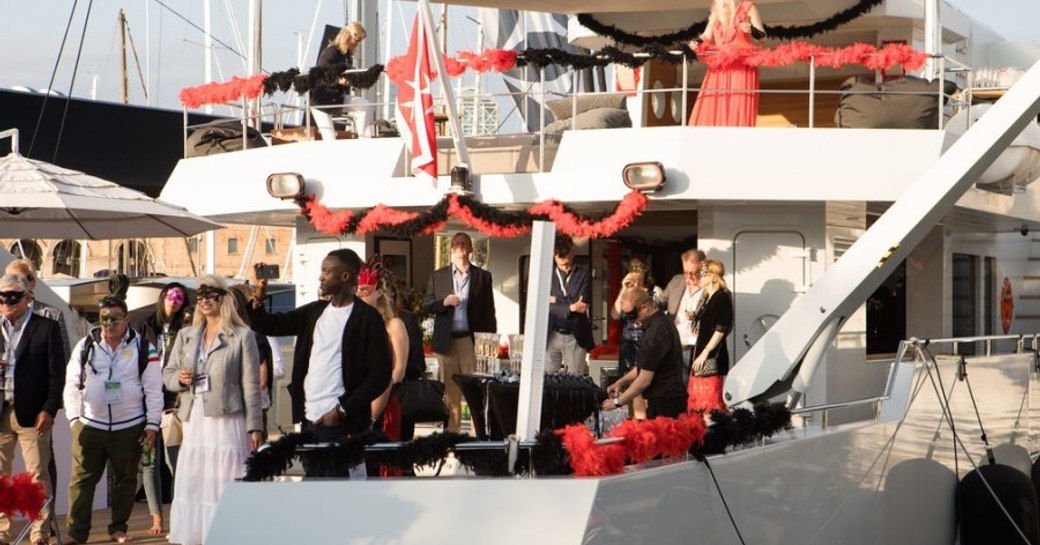 Crew and visitors engaging in a themed mask party onboard motoryacht, with further visitors celebrating dockside adjacent to yacht.