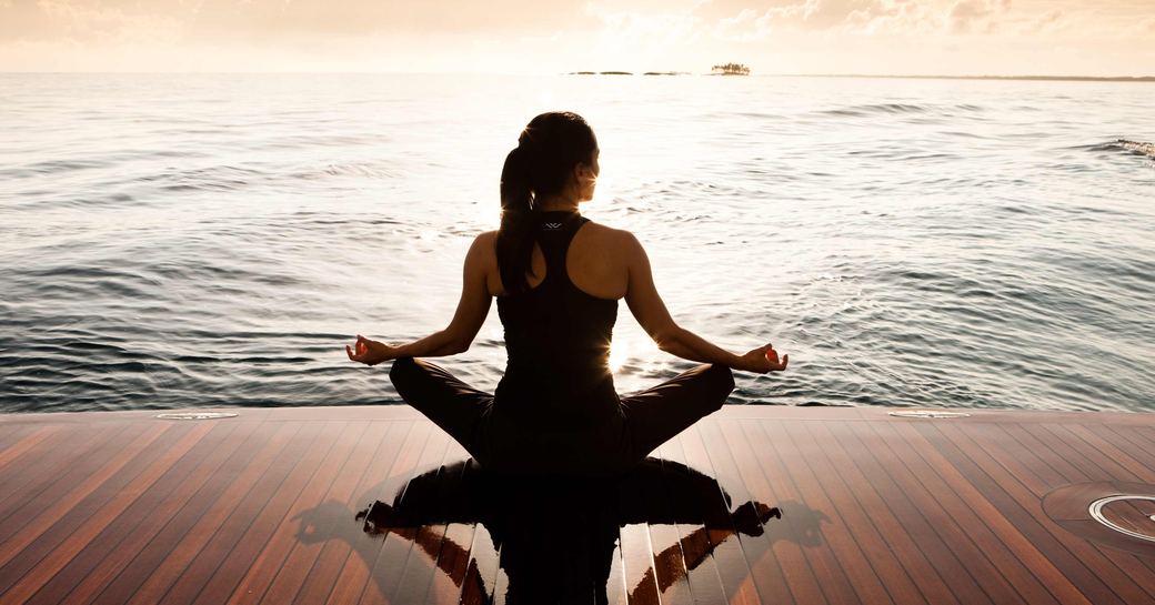 A woman sits crossed legged on a platform off a yacht