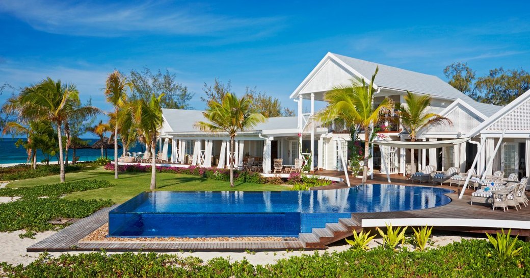 Private island, Thanda Island, shot of villa accommodation and glass-edged infinity pool with palm trees in background and terrace seating around pool