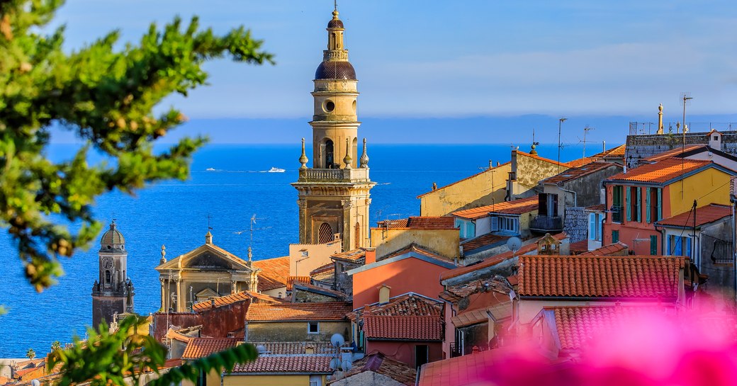 Old town of Menton, French Riviera. Clock tower rising over rooves with sea in background.