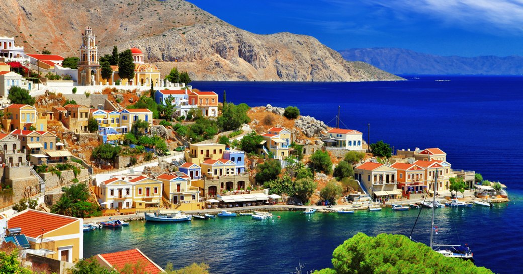 island of symi in greece, coloured buildings and sapphire water, mountain backdrop