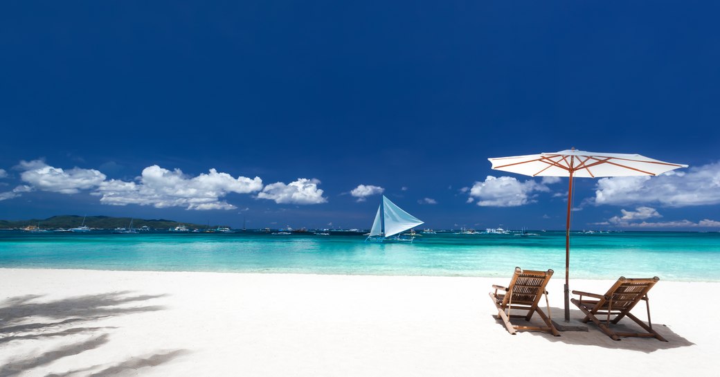 Long stretch of bright white sand beach in the Bahamas, with two deck chairs overlooking the sea